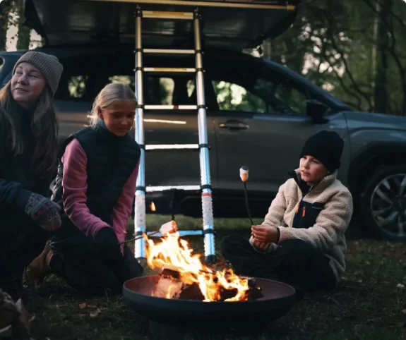 Familj grillar marshmallows vid bil från bilfirma Ronneby, med taktält i skogen.