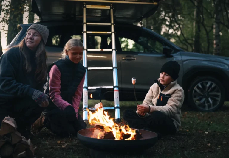 Familj grillar marshmallows vid bil från Bilval Ronneby, med taktält i skogen.