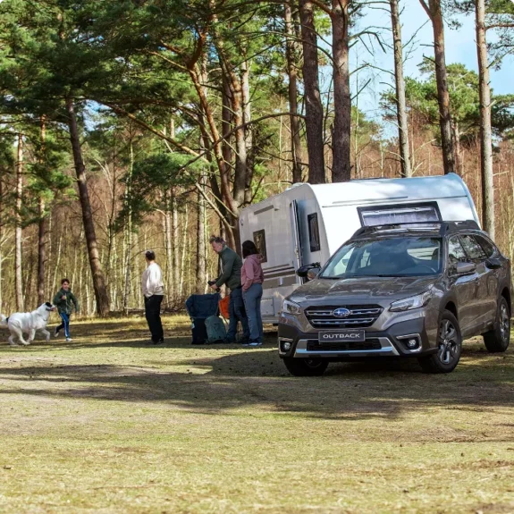 Begagnad bil, en Subaru Outback med husvagn, familj och hund i skogen.