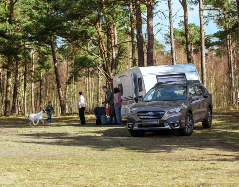 Begagnad bil, en Subaru Outback med husvagn, familj och hund i skogen.